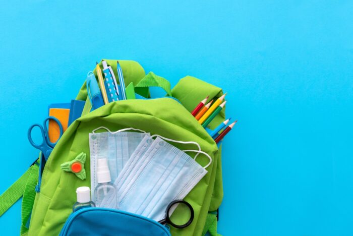 Backpack with school supplies and set of sanitizers and medical protective masks on blue background
