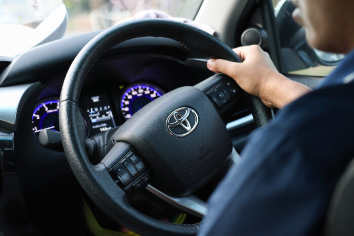 Toyota steering wheel with driver’s hands hold it.