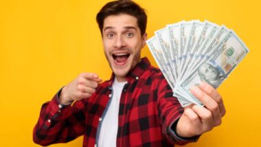 An excited man holding U.S. cash, representing recent settlement checks in the mail.
