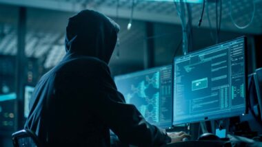 Hooded hacker using a computer, representing the Freecycle data breach.