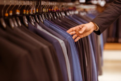 A hand of a modern young handsome businessman choosing classical suit from the row of suits in the suit shop, close-up