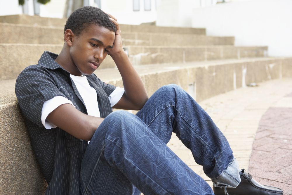 Unhappy Male Teenage Student Sitting Outside On Steps