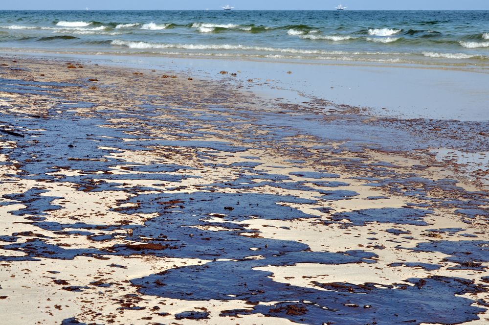 Oil spill on beach with oil skimmers in background.