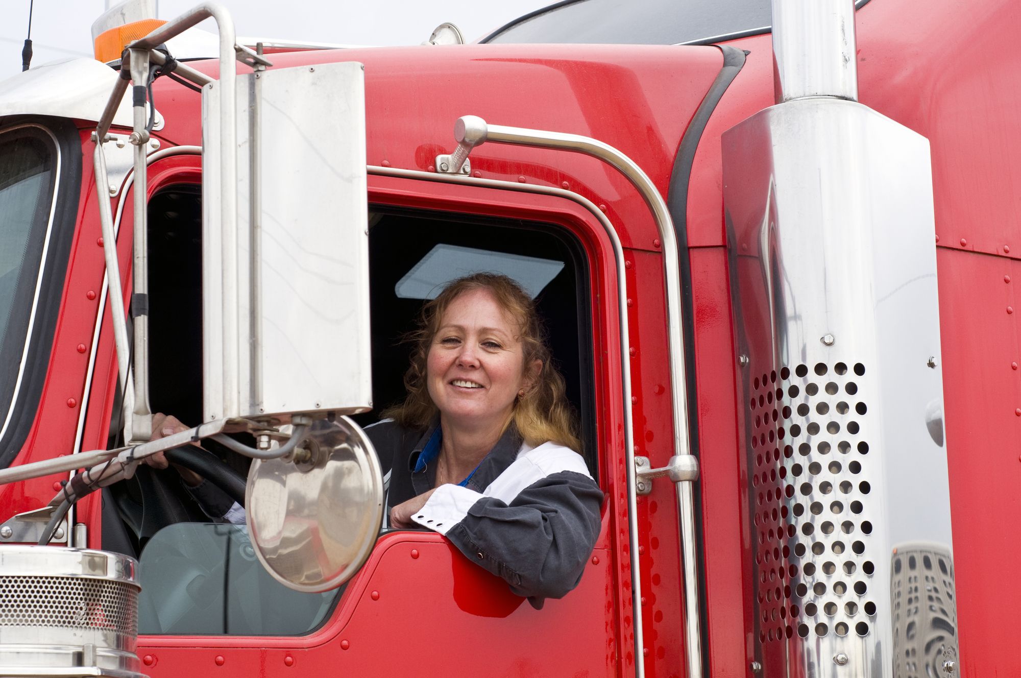 Woman truck driver leaning out the drivers side window. - independent contractor trucker