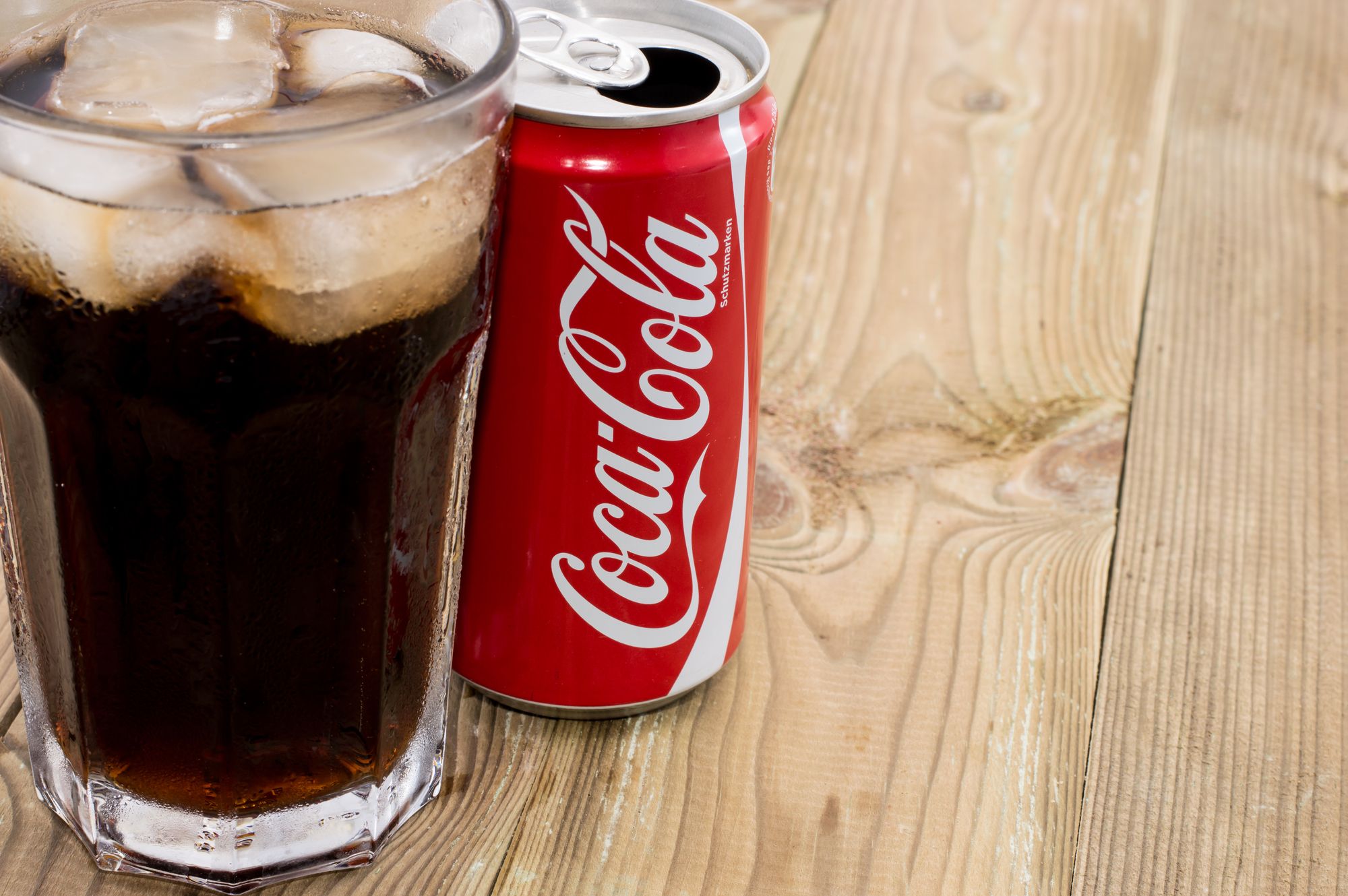 Coca Cola can with Cola in a glass in wooden background