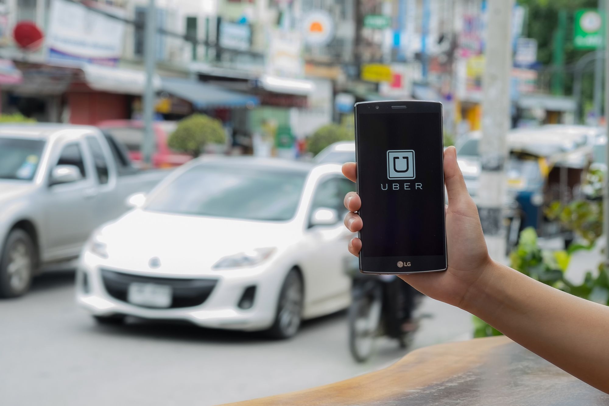 CHIANG MAI,THAILAND - JULY 17, 2016 : A man hand holding Uber app showing on LG G4 on road and red car, Uber is smartphone app-based transportation network.