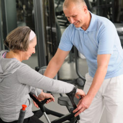 Senior woman with crutches getting help of physiotherapist at gym