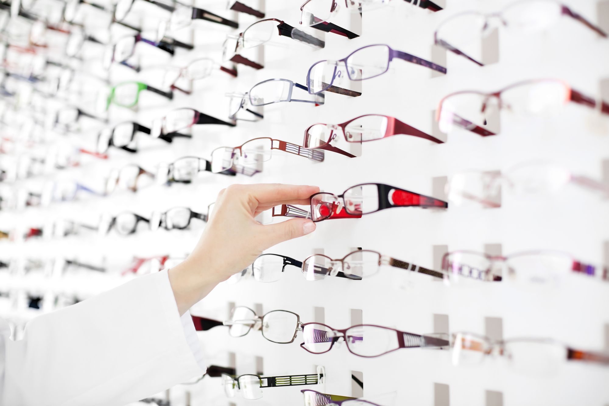 Optician suggest glasses. Closeup showing many eyeglasses in background.