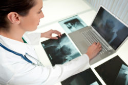 A blond female medical doctor looking at x-rays of hip replacement and using laptop in a hospital