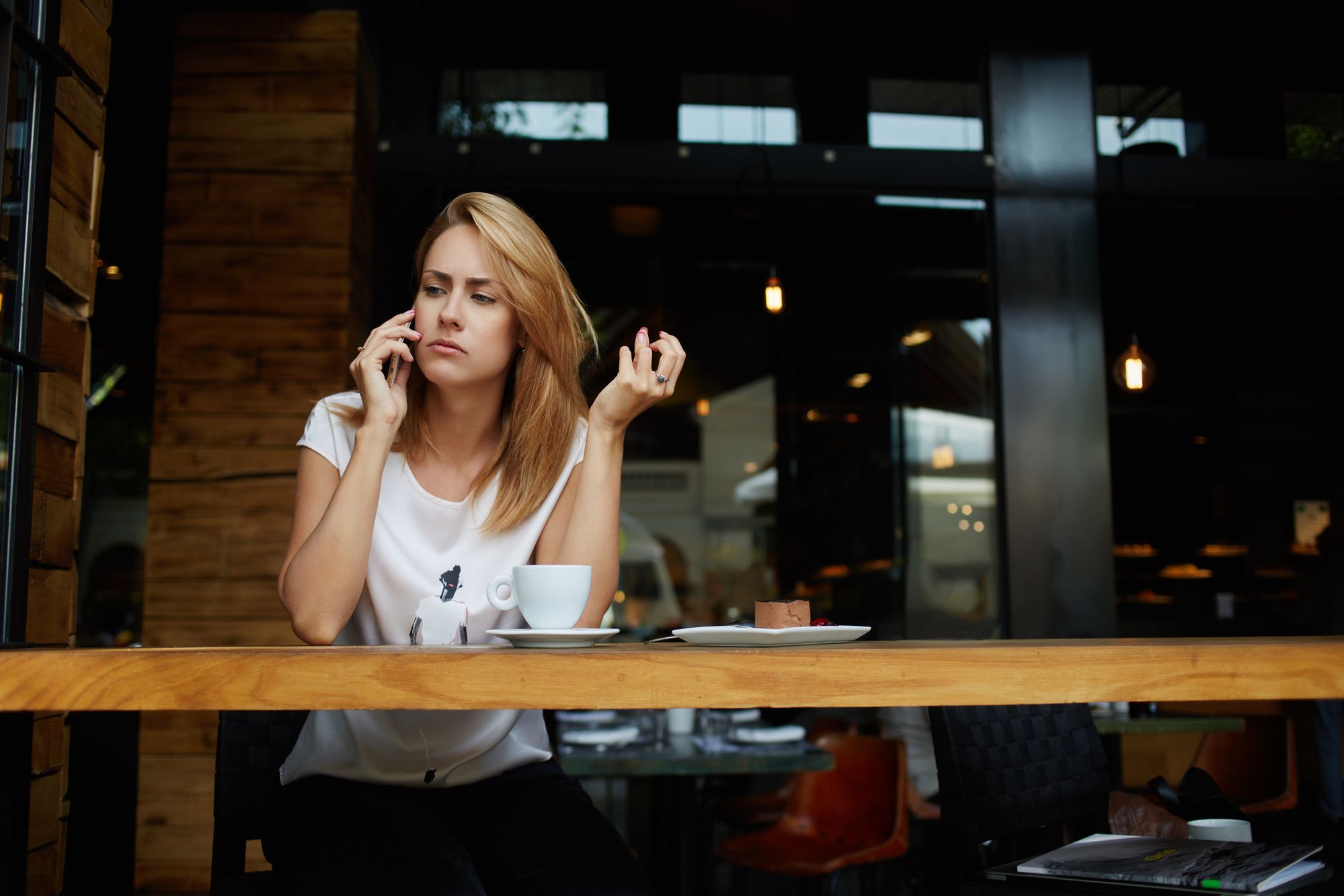 Young upset woman student talking on mobile phone while relaxing in cafe after lectures in University, concerned female have a bad conversation on cell telephone while sitting alone in coffee shop