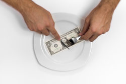 Single one dollar bill on the middle of a plate, knife and fork.