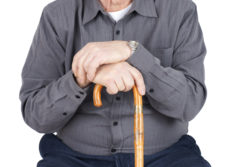 Great detail shot of senior man or elderly sitted and leaning on his cane, focus on hands.
