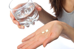 Headache hand with pills medicine tablets ang glass of water against white background