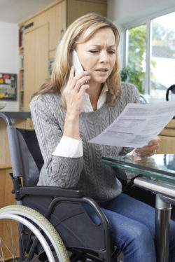 Frustrated Woman In Wheelchair Making Phone Call Whilst Reading Letter