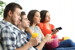 Side view of bored group of four friends watching a bad tv program sitting on a sofa in the livingroom of an apartment