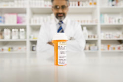 Bottle of pills on desk with a mature male pharmacist in the background