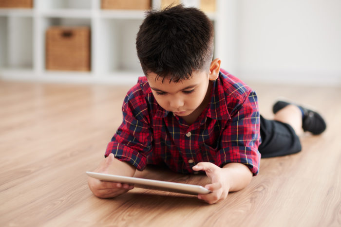 Boy lying lying on the floor and playing game on tablet computer