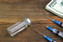 An empty vial and syringes next to money.