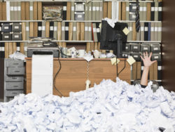 A woman is buried under fax paper in an office.