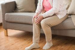 Elderly woman experiencing knee pain while sitting on sofa