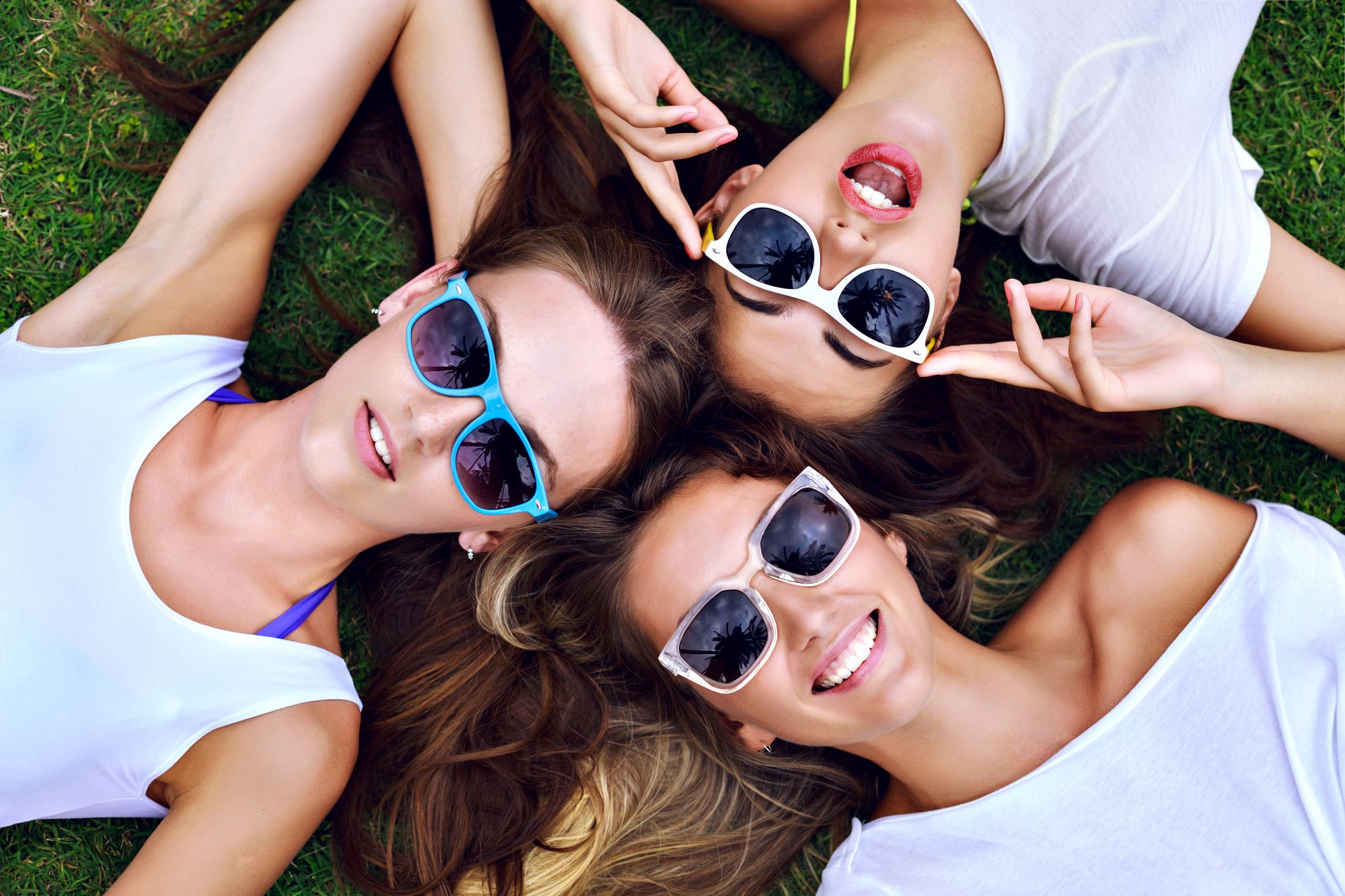 three young women laying on grass wearing Blenders Eyewear sunglasses