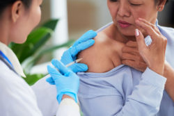 A nurse gives a woman a shot in her shoulder.