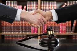 Two lawyers shake hands in front of law books.