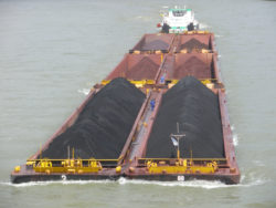 A tug pushes a barge along a river.