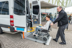 A man in a wheelchair is being helped into a van.
