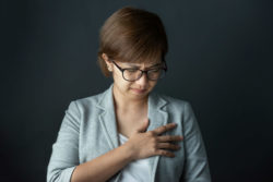 A woman in glasses experiencing chest pain.