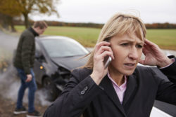 A woman makes a phone call after a car accident.
