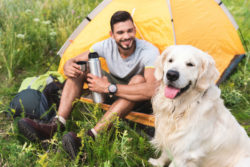 A man sits with his dog outside a tent.