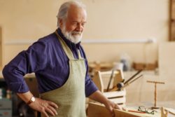 Elderly man wearing carpenter smock with hip pain