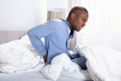 A young man in bed shows signs of back pain.