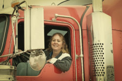 A woman sits in the cab of a semi truck.