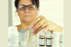 A woman looking at prescription bottles in her medicine cabinet.