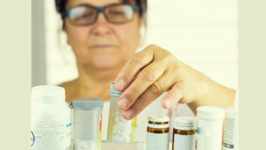 A woman looking at prescription bottles in her medicine cabinet.
