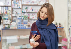 A woman looks up medication on her phone while holding pill bottle.