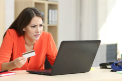 A woman looks concerned while using a laptop and holding a credit card.