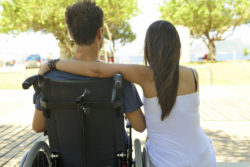 A woman sits next to a man in a wheelchair.