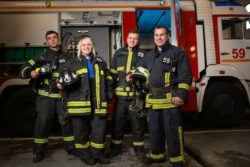 Four firefighters stand next to a fire engine.