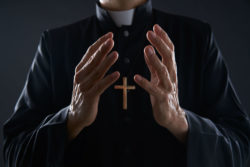 priest praying with open arms for sex abuse victims