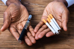 Hands hold e-cigarettes and traditional cigarettes.