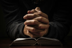 Hands folded in prayer over a bible