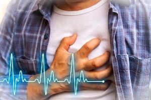 A man in a white t-shirt and blue flannel shirt grabs his chest with his right hand, and a heartbeat graphic overlays the photo - Kombiglyze XR Side Effects