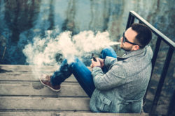 A man vapes by the water.