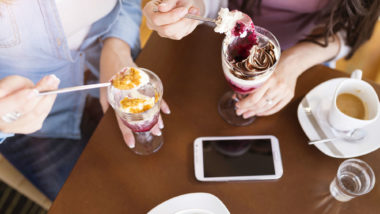Two women eat ice cream at a table.
