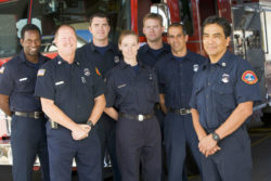 Seven firefighters stand in front of a fire engine.