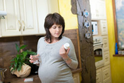 A pregnant woman reads the label on a bottle of vitamins.