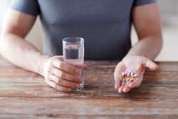 A man holds a glass of water and a handful of pills.